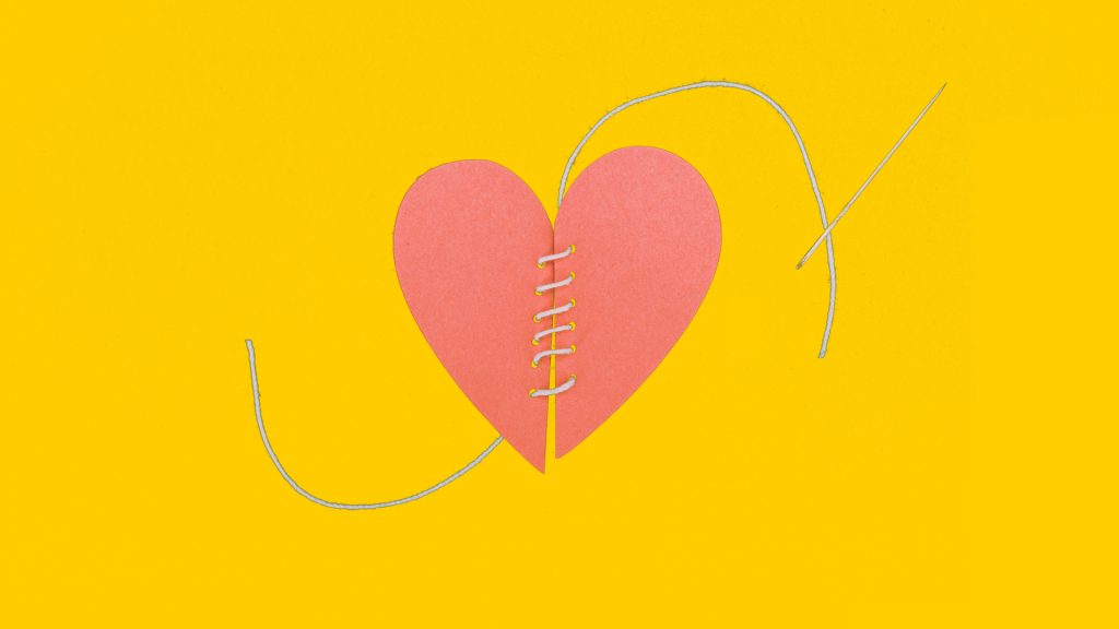 Two halves of a paper heart that are sewn together with a needle and thread